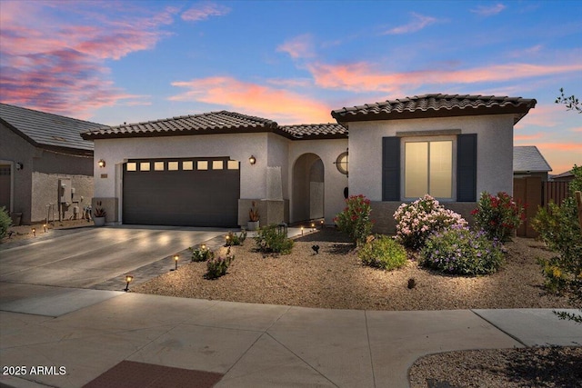 mediterranean / spanish house with concrete driveway, a tiled roof, an attached garage, and stucco siding