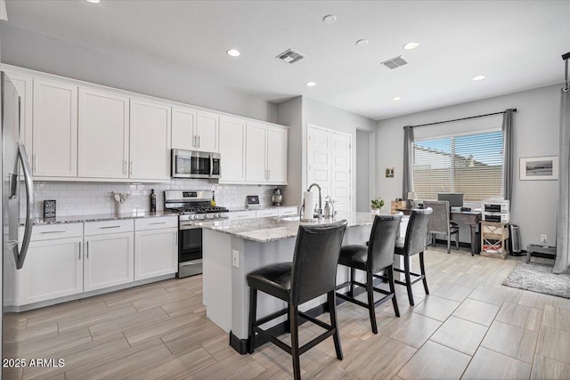kitchen with stainless steel appliances, a sink, light stone countertops, white cabinetry, and recessed lighting