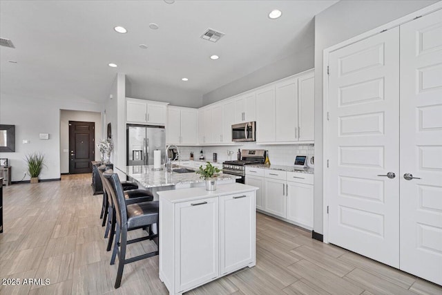 kitchen with appliances with stainless steel finishes, a sink, recessed lighting, white cabinetry, and a breakfast bar area