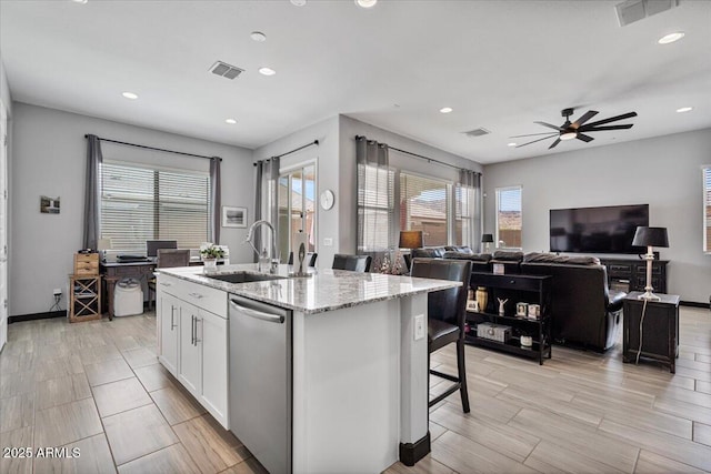 kitchen with a sink, ceiling fan, white cabinets, stainless steel dishwasher, and a kitchen island with sink