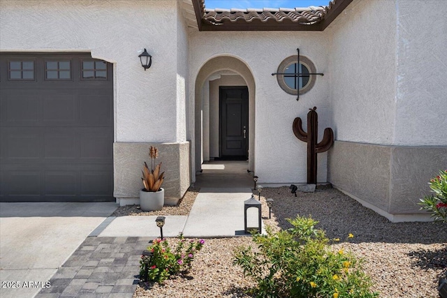 entrance to property featuring stucco siding, an attached garage, and driveway
