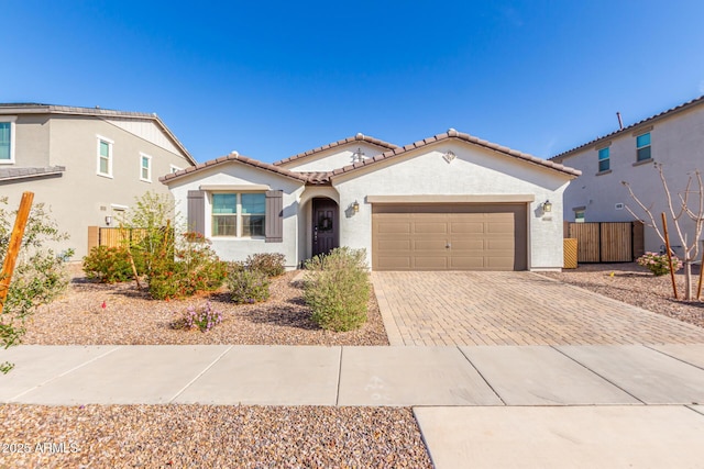 mediterranean / spanish home with fence, an attached garage, stucco siding, a tile roof, and decorative driveway