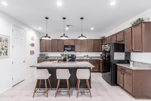 kitchen with visible vents, black appliances, a breakfast bar, a sink, and light stone countertops