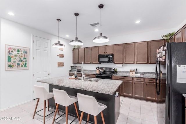 kitchen with visible vents, a kitchen breakfast bar, black appliances, and light stone countertops