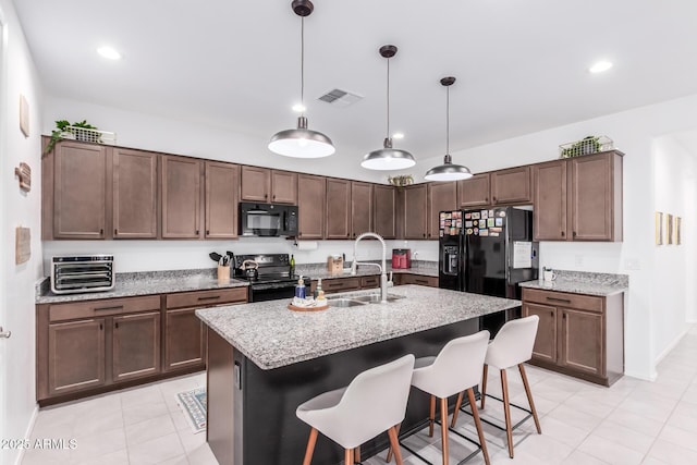 kitchen featuring visible vents, a kitchen breakfast bar, hanging light fixtures, black appliances, and a sink