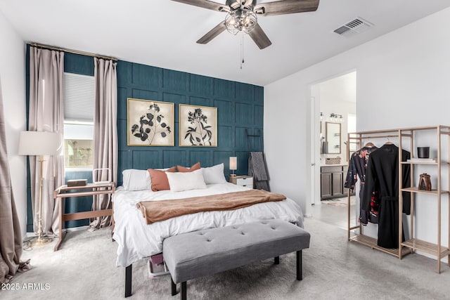 bedroom with visible vents, light carpet, ensuite bathroom, and an accent wall