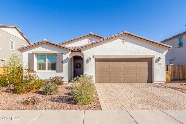 mediterranean / spanish house featuring fence, an attached garage, stucco siding, a tiled roof, and decorative driveway