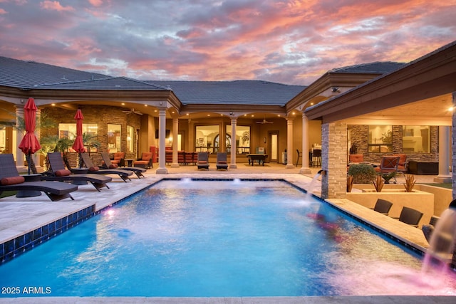 pool at dusk featuring ceiling fan, pool water feature, and a patio