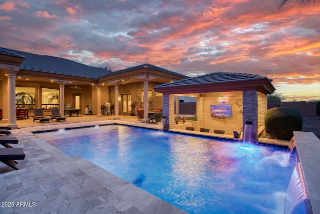 pool at dusk with pool water feature, a patio area, an outdoor living space, and ceiling fan