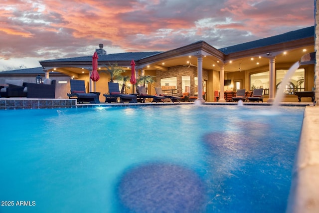 pool at dusk featuring pool water feature and a patio