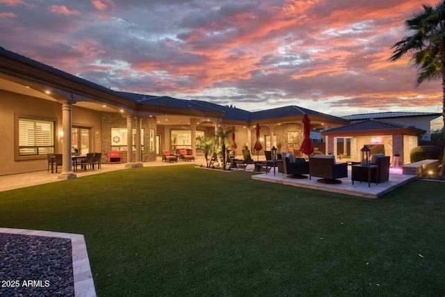 back house at dusk featuring a patio area, outdoor lounge area, and a yard