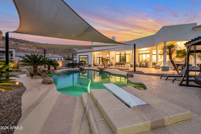 pool at dusk with a diving board and a patio