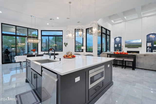 kitchen featuring sink, light stone counters, an island with sink, decorative light fixtures, and appliances with stainless steel finishes