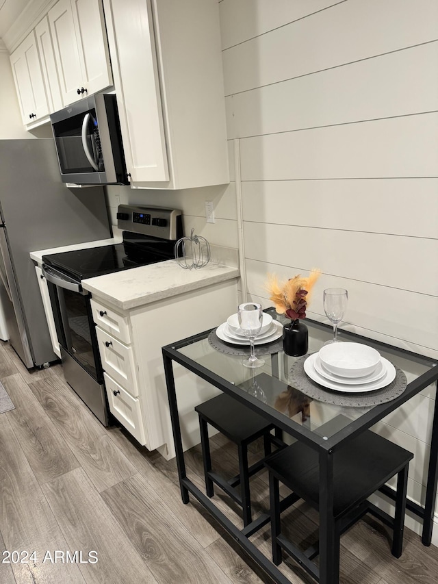 kitchen featuring light stone countertops, light wood-type flooring, stainless steel appliances, white cabinets, and wood walls