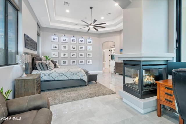 bedroom featuring a multi sided fireplace and a raised ceiling