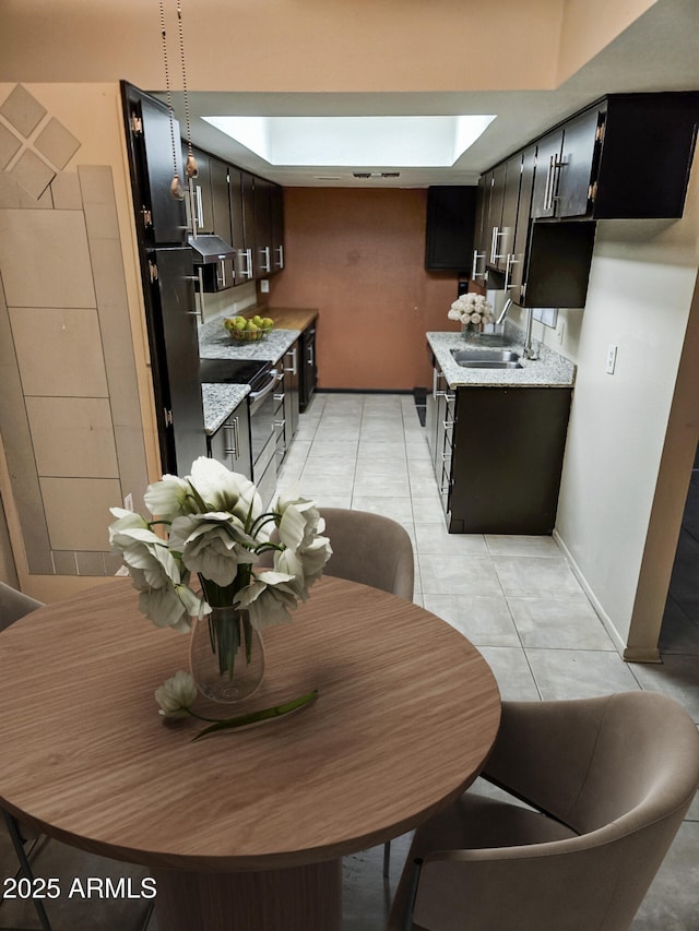 kitchen with a skylight, sink, stainless steel range with electric cooktop, light tile patterned floors, and light stone counters