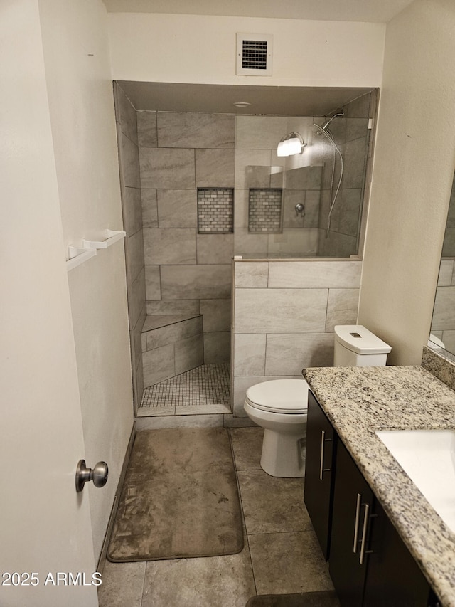 bathroom with vanity, tiled shower, and toilet