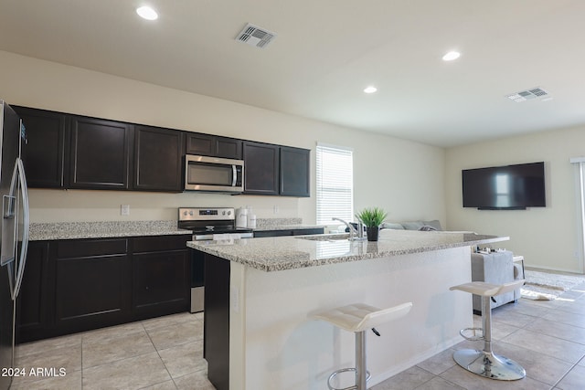 kitchen with a kitchen breakfast bar, sink, an island with sink, light stone counters, and stainless steel appliances