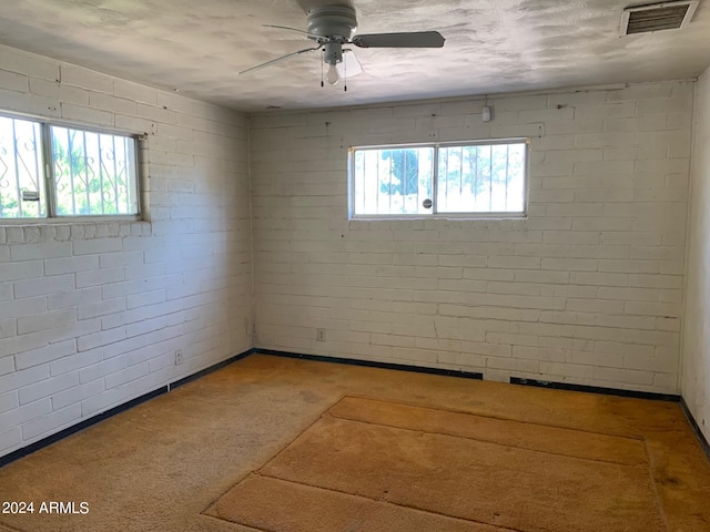 spare room featuring ceiling fan, brick wall, and a healthy amount of sunlight