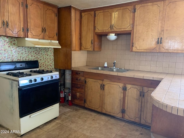 kitchen featuring tile counters, sink, white gas stove, and tasteful backsplash