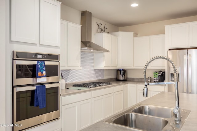 kitchen with appliances with stainless steel finishes, light countertops, wall chimney range hood, white cabinetry, and a sink