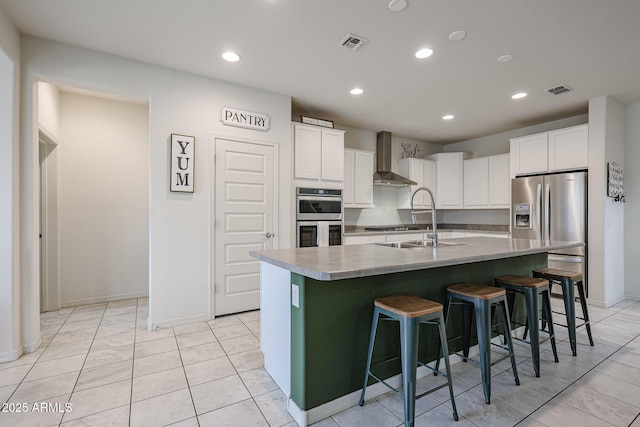 kitchen featuring wall chimney range hood, a center island with sink, white cabinets, and light countertops