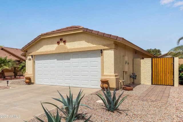 view of front of house with stucco siding, a gate, a tiled roof, and concrete driveway