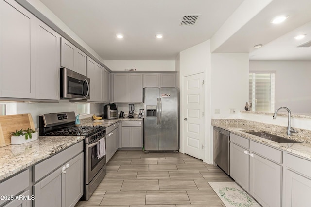 kitchen featuring light stone countertops, appliances with stainless steel finishes, a sink, gray cabinets, and visible vents