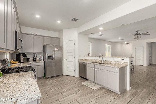 kitchen featuring a sink, appliances with stainless steel finishes, a peninsula, and gray cabinetry