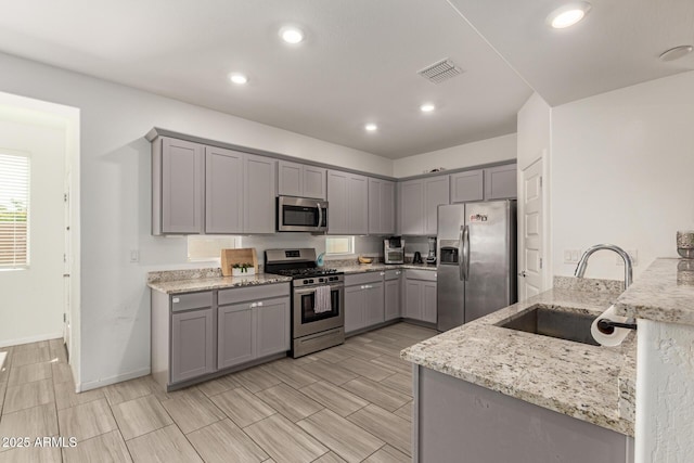 kitchen with visible vents, light stone countertops, gray cabinets, a sink, and stainless steel appliances