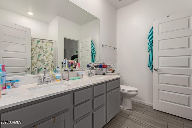 bathroom featuring double vanity, toilet, a sink, and wood finished floors
