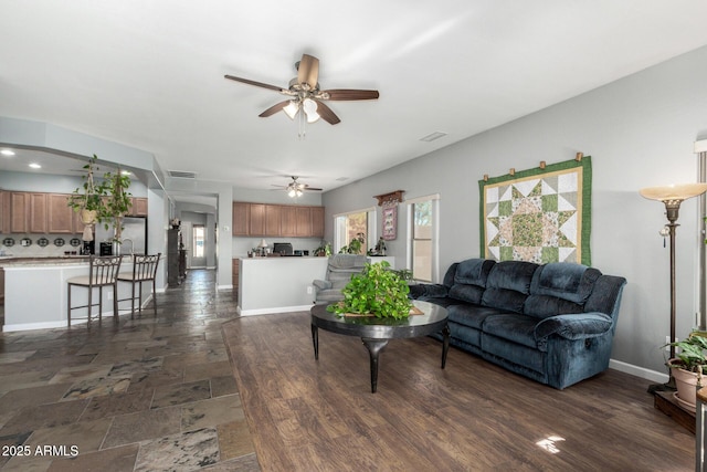 living area with a ceiling fan, stone finish floor, a wealth of natural light, and baseboards