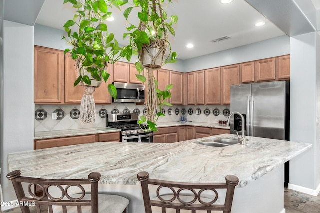 kitchen featuring tasteful backsplash, visible vents, appliances with stainless steel finishes, a kitchen breakfast bar, and a sink