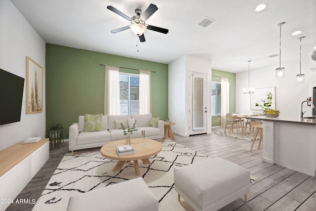 living room featuring ceiling fan with notable chandelier, baseboards, visible vents, and wood tiled floor