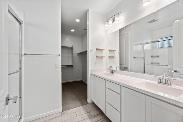 bathroom featuring a shower with door, wood finished floors, a sink, and visible vents