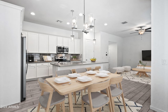 kitchen with decorative backsplash, stainless steel appliances, a center island with sink, decorative light fixtures, and light hardwood / wood-style floors