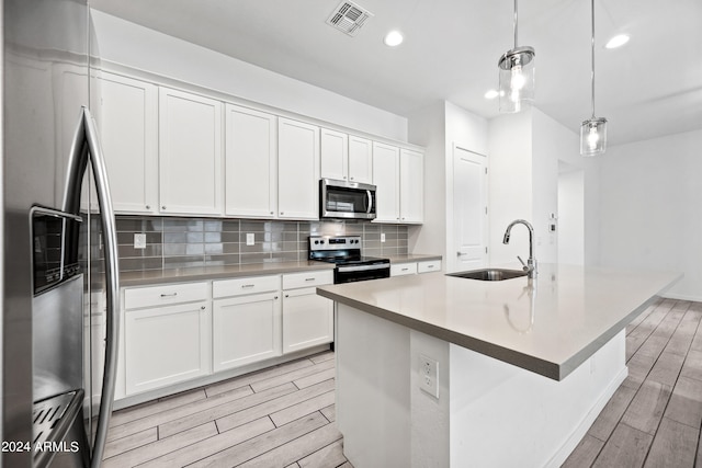 kitchen with sink, hanging light fixtures, stainless steel appliances, white cabinets, and a kitchen island with sink