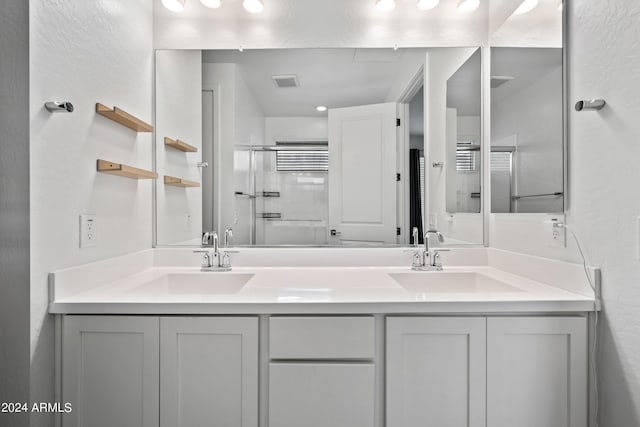 bathroom with double vanity, a shower with door, visible vents, and a sink