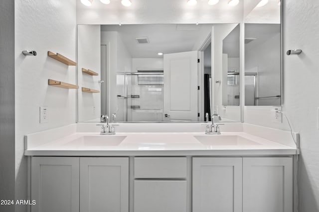 bathroom with double vanity, visible vents, a sink, and a shower with door