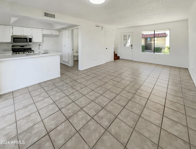 kitchen with light tile patterned floors, sink, a textured ceiling, white cabinetry, and stainless steel appliances