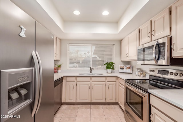 kitchen featuring a tray ceiling, sink, appliances with stainless steel finishes, and light tile patterned flooring