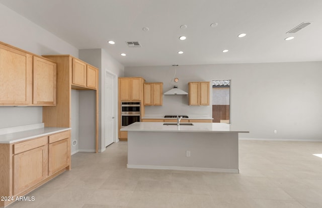 kitchen with extractor fan, stainless steel double oven, light brown cabinetry, and an island with sink