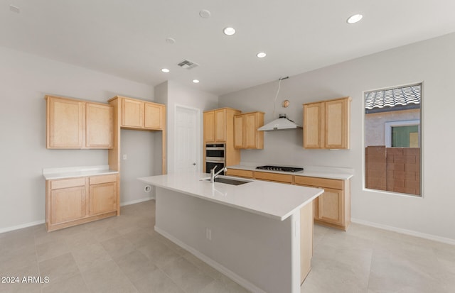 kitchen with gas stovetop, double oven, light brown cabinets, a kitchen island with sink, and sink