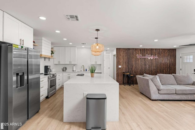 kitchen with pendant lighting, white cabinetry, appliances with stainless steel finishes, and light hardwood / wood-style flooring