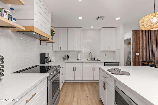 kitchen featuring electric stove, sink, hanging light fixtures, white cabinets, and light wood-type flooring