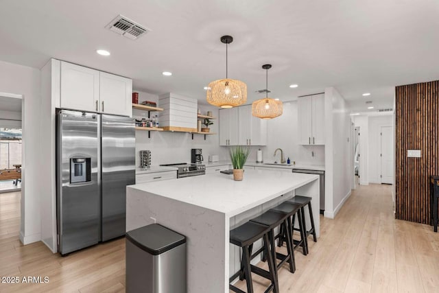 kitchen with white cabinetry, decorative light fixtures, a kitchen island, and appliances with stainless steel finishes