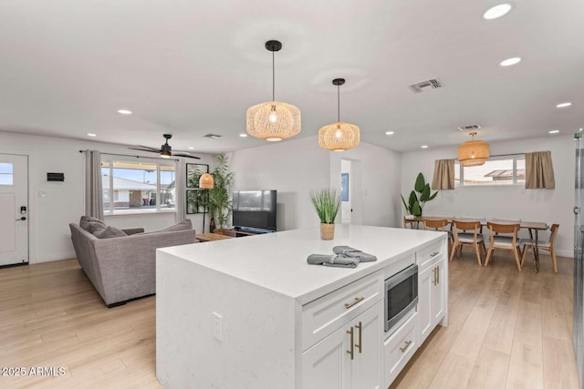 kitchen featuring white cabinetry, stainless steel microwave, decorative light fixtures, and light wood-type flooring