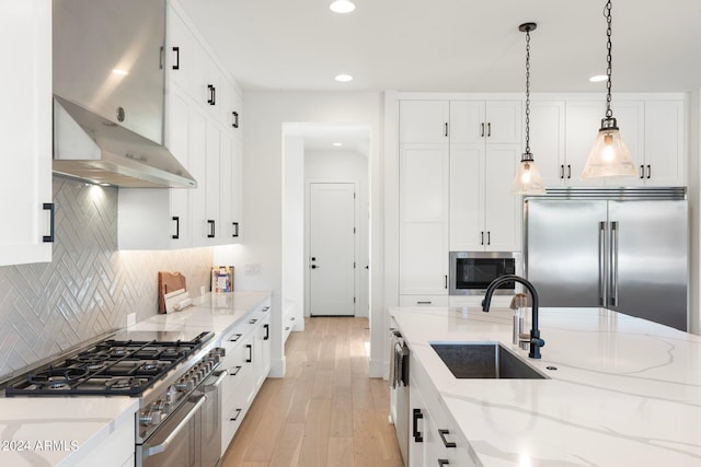 kitchen featuring white cabinetry, sink, wall chimney exhaust hood, built in appliances, and pendant lighting