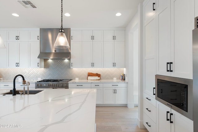 kitchen with sink, hanging light fixtures, wall chimney range hood, decorative backsplash, and high end stainless steel range