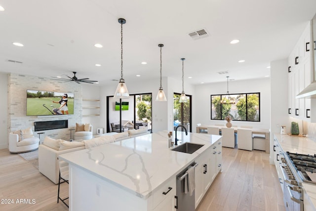 kitchen with a large island with sink, light stone counters, white cabinetry, and sink